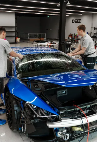 Two DEIZ technicians working on a blue Lamborghini Huracán in the DEIZ workshop